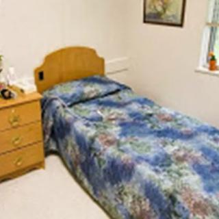 A cozy bedroom featuring a single bed with a floral comforter, a bedside dresser, and wall art.