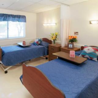 A well-lit hospital room with two patient beds and bedside tables, featuring a calm and welcoming atmosphere.