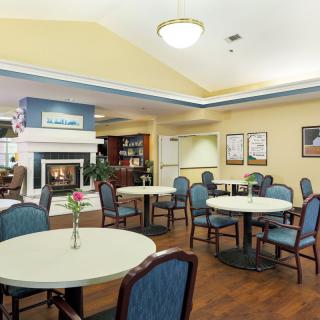 A cozy community dining area with round tables, blue chairs, and a fireplace.