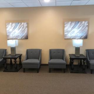 A waiting room with several chairs and lamps arranged neatly along the wall, featuring abstract artwork.