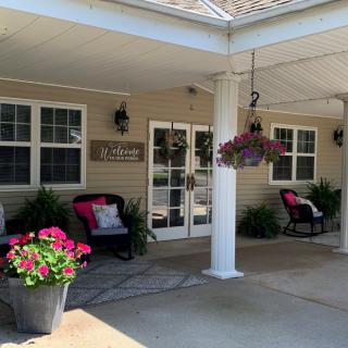 The entrance of a building featuring a porch with seating and flower arrangements.