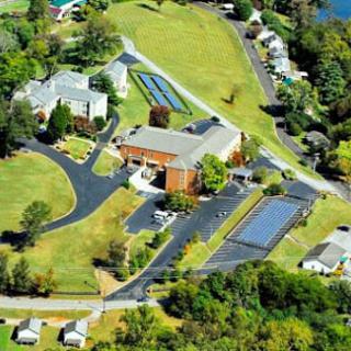 Aerial view of a complex featuring buildings, roads, and solar panels surrounded by greenery.