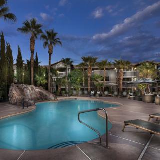 A serene nighttime view of a resort swimming pool surrounded by palm trees and lounge chairs.