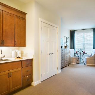 A cozy apartment interior with a small kitchen and a bright living area with seating by the window.