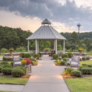 A scenic garden with a central gazebo surrounded by lush greenery and benches.