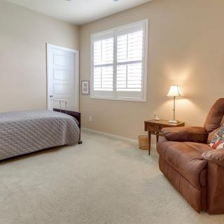 A cozy bedroom with a single bed, an armchair, and a nightstand under soft lighting.