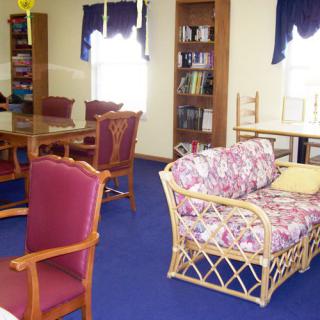 A cozy reading room with bookshelves, a sofa, and chairs on a blue carpet.