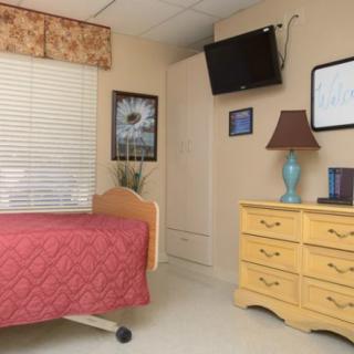 A cozy hospital room with a bed, dresser, and mounted television.