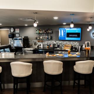 A modern bar interior with a counter, several stools, and a television mounted on the wall.