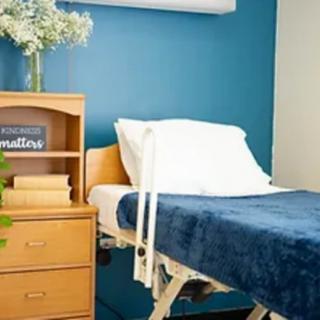A neatly arranged room with a hospital bed, nightstand, and decorative flowers.