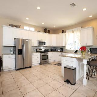 A modern kitchen with stainless steel appliances and white cabinets, featuring a tiled floor and counter seating.
