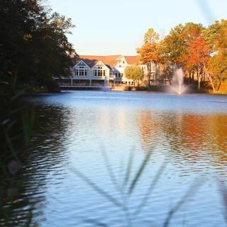 A serene lake view with autumn-colored trees, a fountain, and a distant building reflecting on the water.