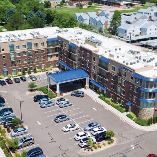 Aerial view of a modern apartment complex with a parking lot and surrounding landscape.