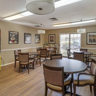 A cozy dining room with multiple tables and chairs, decorated with framed pictures and illuminated by ceiling lights.