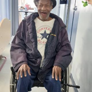 An elderly man in a wheelchair, smiling warmly while dressed in a cozy coat.