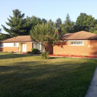 A suburban brick house with a spacious yard and surrounding trees.