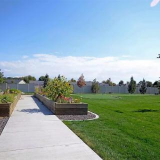 A serene park pathway bordered by lush green grass and garden beds under a clear blue sky.