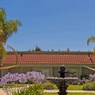 A charming house with a red-tiled roof, surrounded by a garden featuring a central fountain and palm trees.