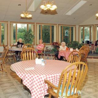 An indoor dining room with elderly people sitting at tables covered with checkered tablecloths.