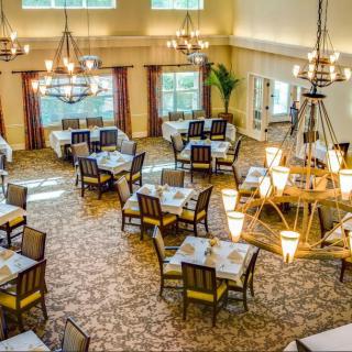A spacious dining room with elegantly arranged tables and chairs, featuring large chandeliers and a carpeted floor.