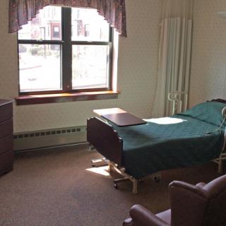 A hospital room with a bed, chair, and window.