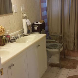 A bathroom with a sink and vanity, equipped with a toilet chair and curtain.