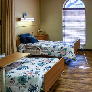 A hospital room featuring two beds with floral patterned bedding and a spacious window.