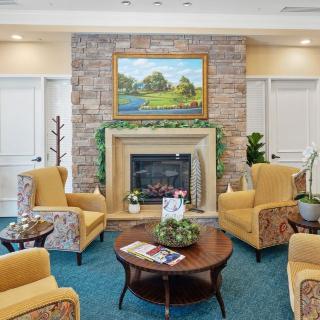 A cozy living room with a modern fireplace, surrounded by comfortable chairs, artwork above the mantel, and a coffee table in the center.