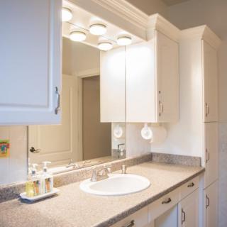 A clean and well-lit bathroom with a sink, mirror, and white cabinets.