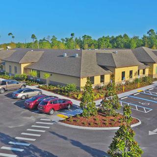 A view of a building complex with a parking lot and cars, surrounded by trees under a clear blue sky.