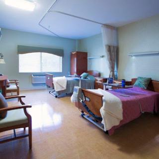 A well-lit and clean hospital patient room featuring two beds and seating.