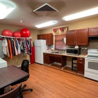 A multi-purpose room featuring a kitchen area, clothes rack with hanging garments, and exercise balls.