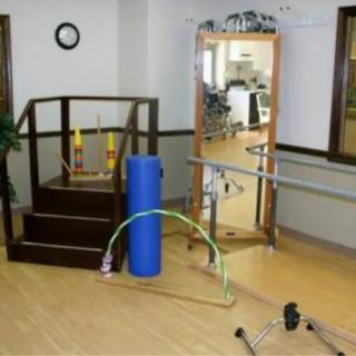 A physical therapy room equipped with various rehabilitation tools, including stairs, a balance beam, mirrors, and exercise equipment.