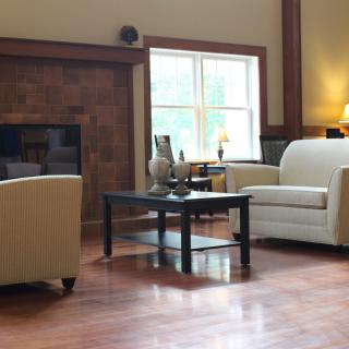 A cozy living room with a sofa, armchair, and coffee table, featuring a fireplace and hardwood flooring.