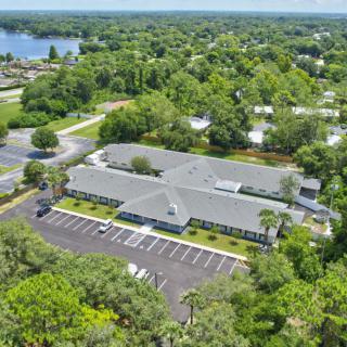 Aerial view of a building complex surrounded by lush greenery and a parking lot.