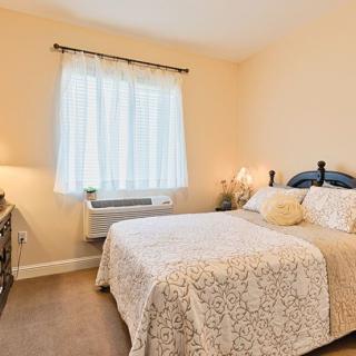 A cozy bedroom with a neatly made bed, soft lighting, and a window letting in natural light.