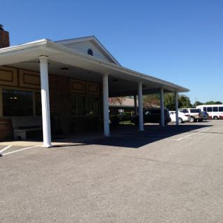 A view of a building featuring a covered entrance and parked vehicles in a sunny outdoor setting.