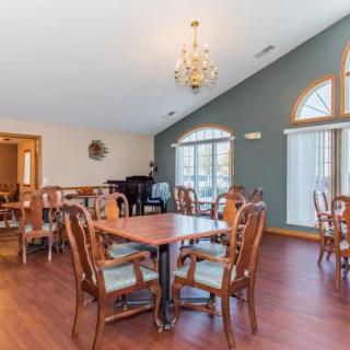 A spacious dining room featuring multiple tables and chairs, a chandelier, hardwood flooring, large windows, and a piano in the corner.