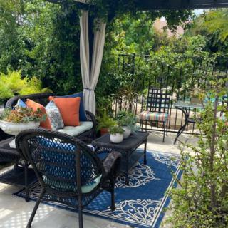 A cozy outdoor patio with comfortable seating, vibrant cushions, and lush greenery.