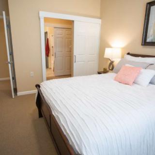 A cozy bedroom with a large bed featuring white bedding and decorative pillows, illuminated by a bedside lamp.