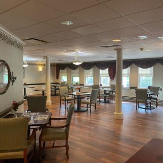 A cozy dining area with neatly arranged tables and chairs, featuring large windows and elegant curtains.