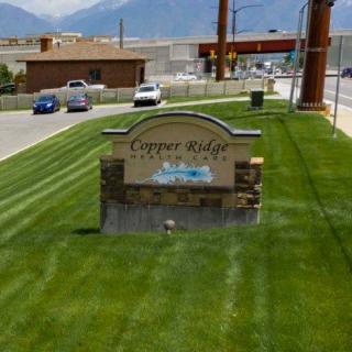 A sign for Copper Ridge Auto Spa located on a grassy area beside a road with buildings and mountains in the background.