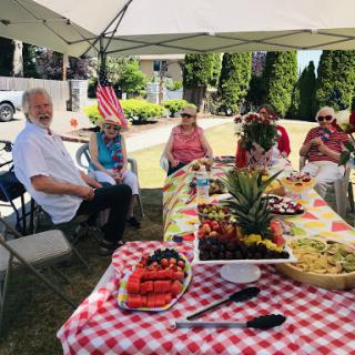 A joyful outdoor gathering with friends, enjoying a spread of delicious fruits and food under a sunny sky.