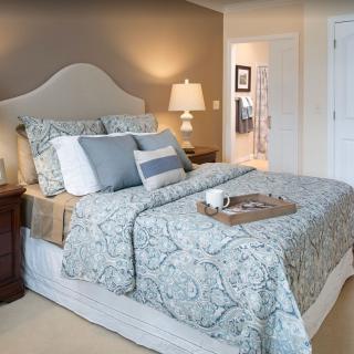 A cozy and elegantly designed bedroom with a neatly made bed, decorative pillows, a nightstand, and a lamp.