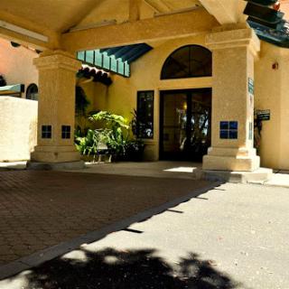 A welcoming entrance to a beautifully designed building, surrounded by lush greenery and illuminated by sunlight.