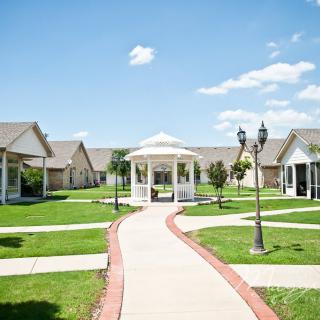 A scenic view of a gazebo surrounded by cottages and manicured lawns under a clear blue sky.