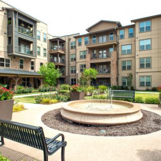 A modern apartment complex featuring a central courtyard with a fountain and outdoor seating.