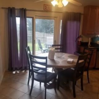 A cozy dining area with a round table and chairs next to a sliding glass door with purple curtains.