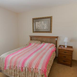 A cozy bedroom with a striped bedspread and a nightstand featuring a lamp, set beneath a framed painting.