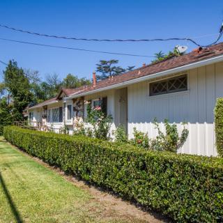 A quaint residential house with a well-maintained hedge and lawn under a clear blue sky.